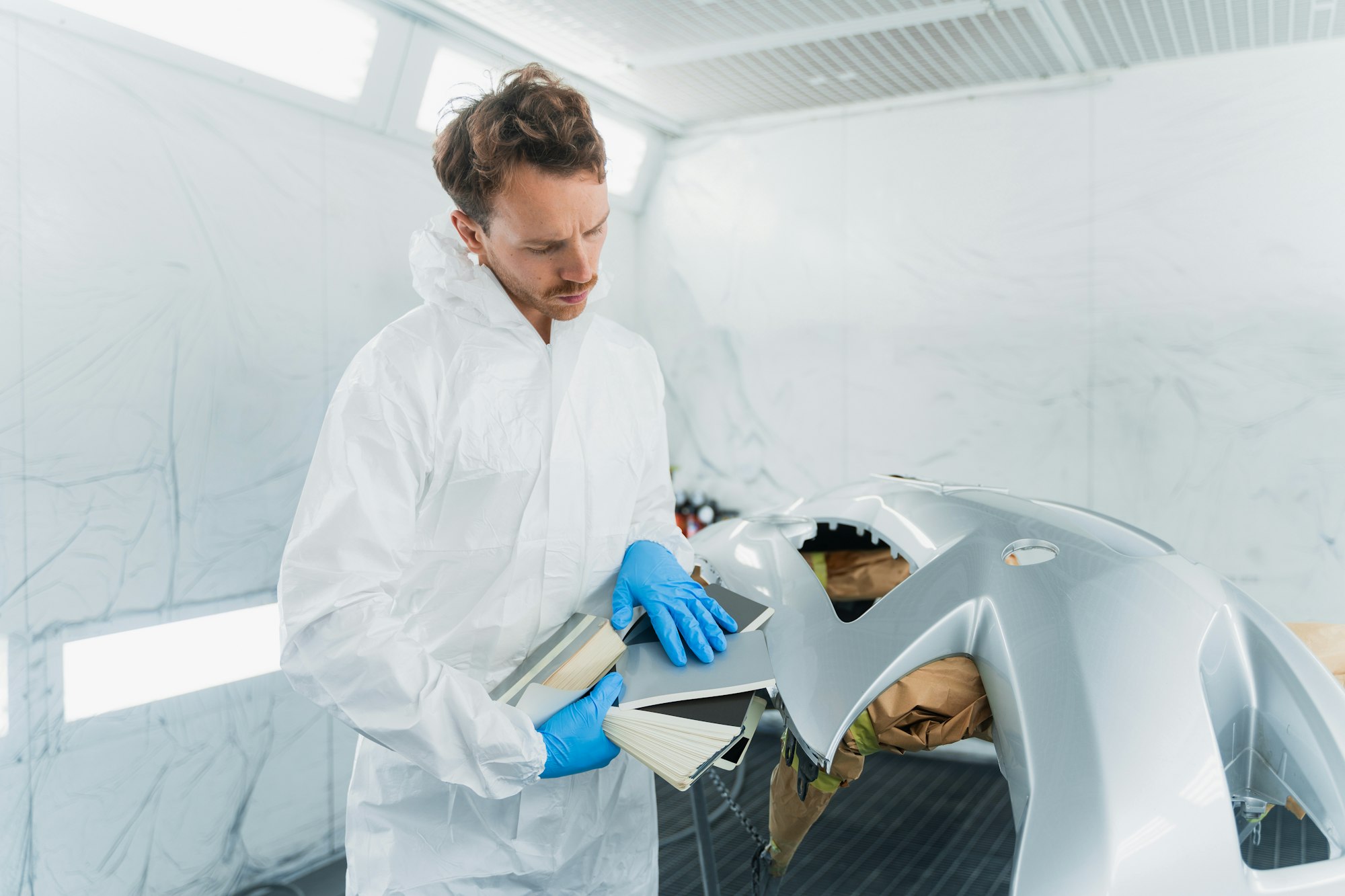Young male car body repair worker in vehicle painting booth
